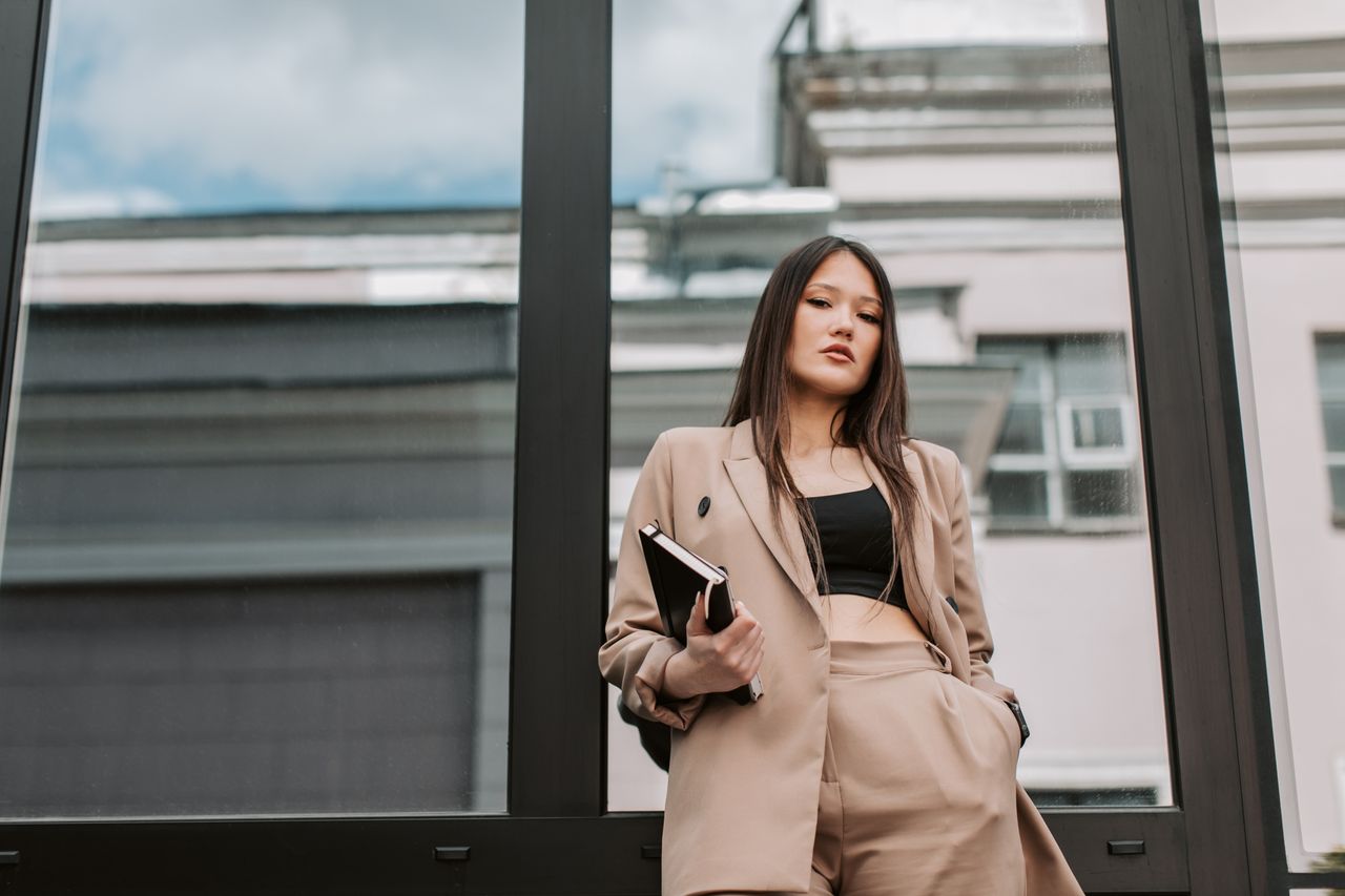why-choose-us Stylish Asian woman in sharp corporate attire posing confidently against a glass wall.