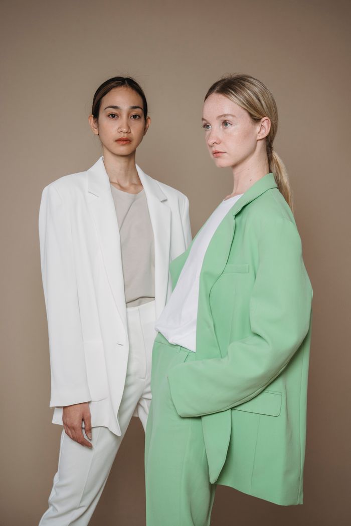 Services-01 Fashionable portrait of two women wearing green and white suits on a beige background.