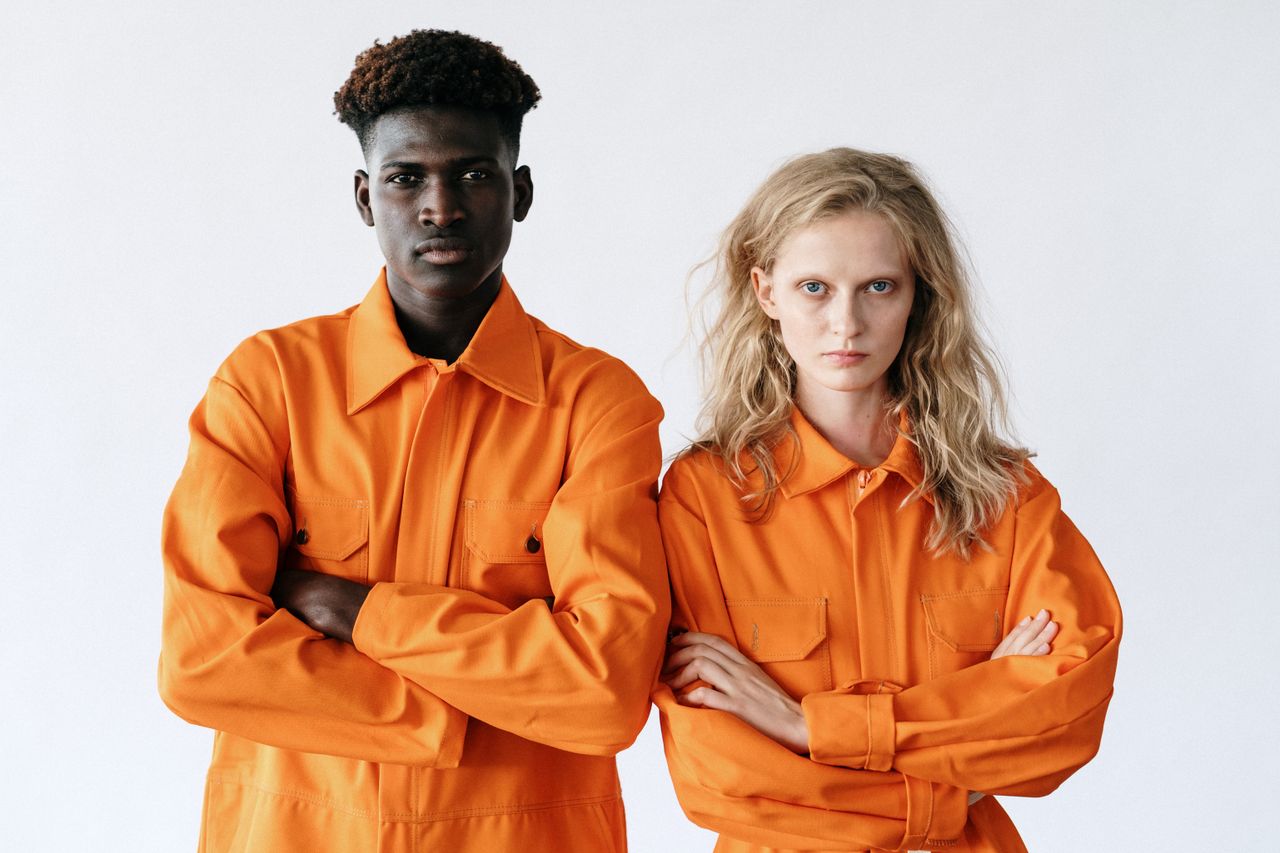 digital Portrait of a diverse pair in vibrant orange work uniforms with determined expressions.